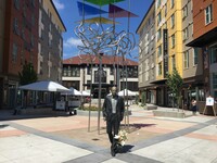  Bronze statue of man in the center of a plaza, striding forward with apartment buildings on either side.