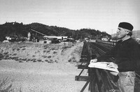  A man standing outdoors and drawing on a sketch pad propped on a wooden fence.