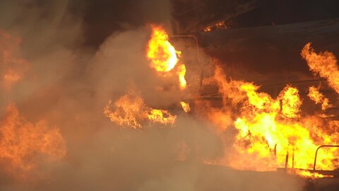 Flames engulfing charred skeleton of train cars that were carrying chemicals.